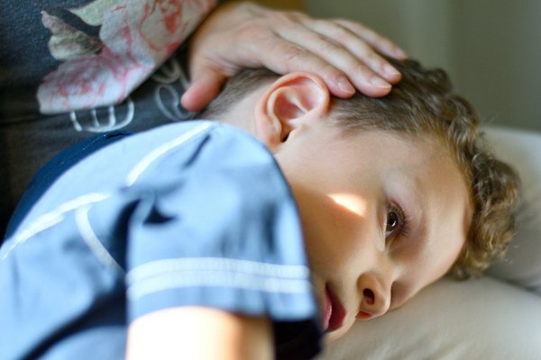 Hand liegt sanft auf dem Kopf eines liegenden Jungen