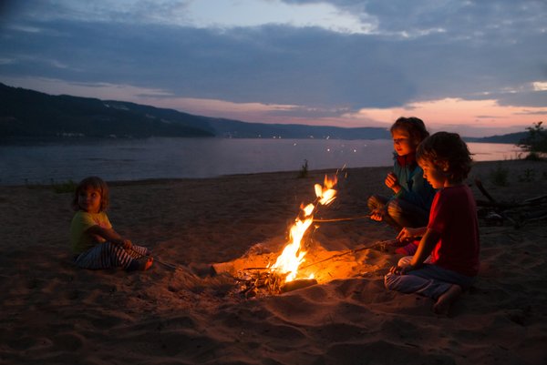 Kinder sitzen am Strand um Feuer