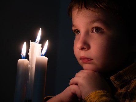 Junge nachdenklich vor drei brennenden Kerzen