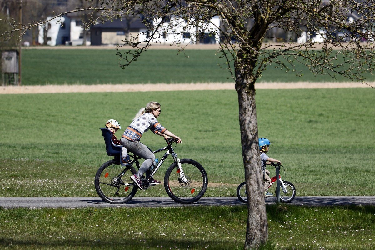 Frau auf Velo mit Kindersitz, Kind mit Kindervelo fährt voraus